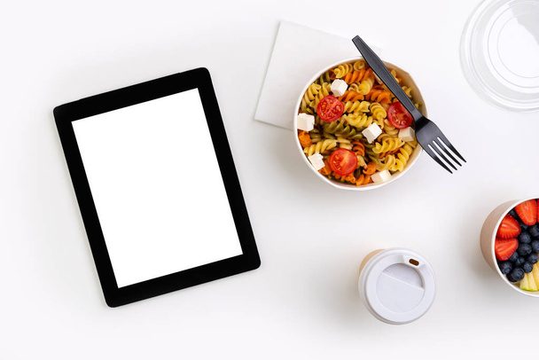 Comida en cajas para llevar en mesa blanca con tableta con pantalla en blanco. Entrega de comida en línea. Nuevo concepto de trabajo normal desde el hogar
. - Foto, imagen