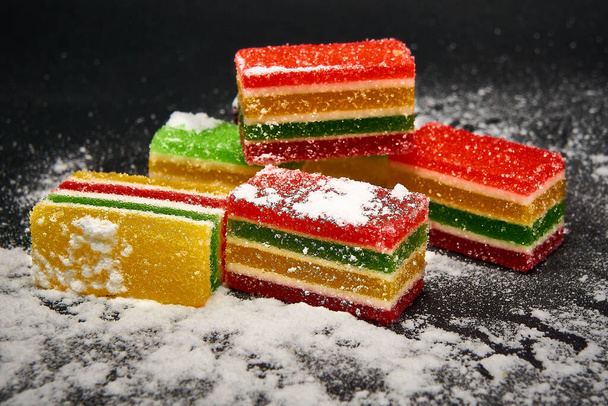 Slices of marmalade in icing sugar on a black background - Photo, Image