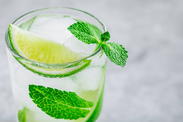 Mojito cocktail with ice, fresh mint and lime in glass on gray stone background. Refreshing ice cold summer drink. - Фото, зображення