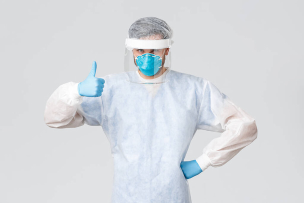 Covid-19, pandemic, healthcare workers fighting virus outbreak. Confident and determined medical worker in personal protective equipment, show thumb-up, protect people lives - Photo, Image