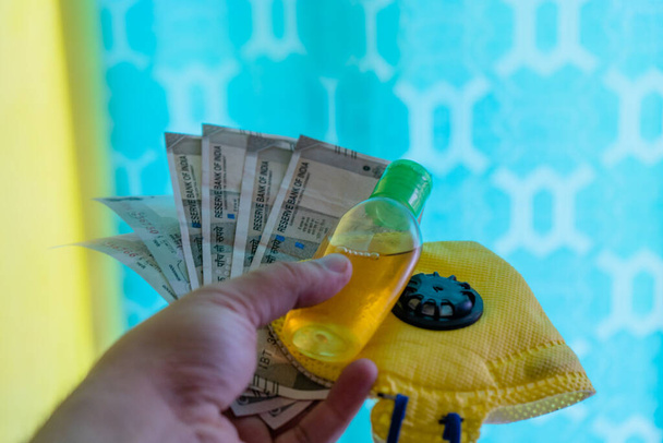 Раздача индийских банкнот, желтой маски и дезинфицирующего средства, на красочном фоне
 - Фото, изображение