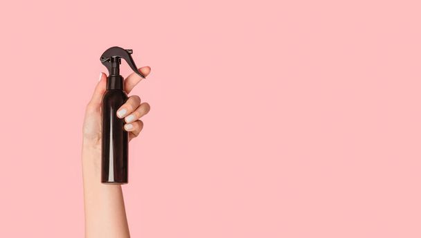 Cropped view of girl hand showing black spray bottle with cosmetic product on pink background, copy space - Foto, imagen