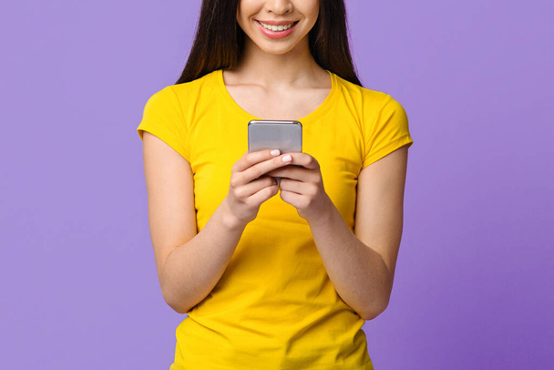 Moderni älypuhelin käsissä tunnistamaton aasialainen tyttö seisoo violetti tausta - Valokuva, kuva