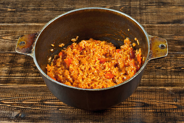 Pilaf with meat and carrots in an old cast iron cauldron. Rice on a brown shabby board. - Valokuva, kuva