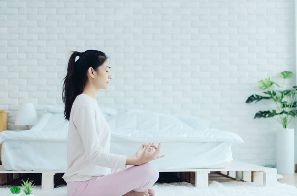 Азиатские девушки сидя на представлениях yoga в постели в теплом morning.Warm tone.Do не сосредоточиться на предметах
. - Фото, изображение