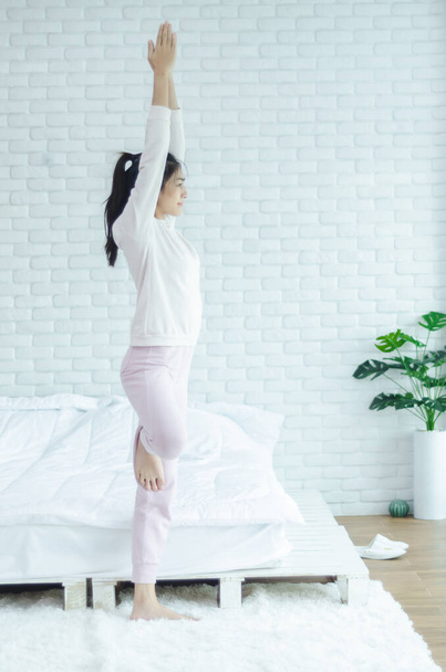 Азиатские девушки сидя на представлениях yoga в постели в теплом morning.Warm tone.Do не сосредоточиться на предметах
. - Фото, изображение