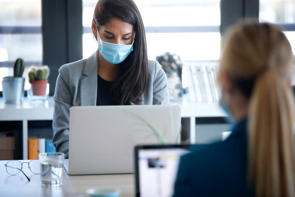 Shot of two business women wearing a hygienic face mask while work with laptops in the coworking space. Social distancing concept. - Foto, immagini