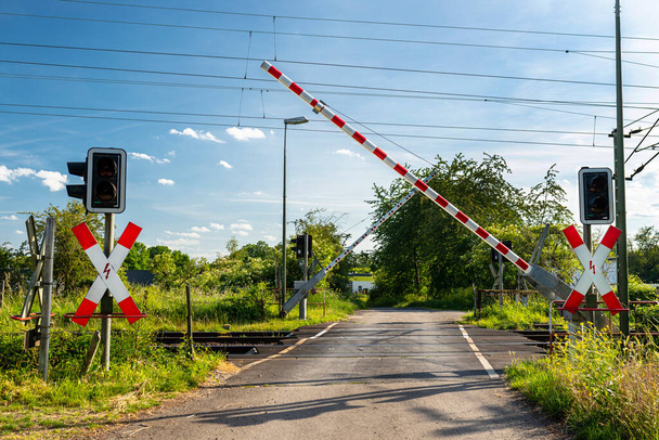 Travessia de ferrovia vigiada com barreiras de fechamento, luz de advertência vermelha e cruz de Santo André
. - Foto, Imagem