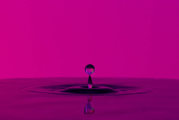 Капля жидкости брызгает на тихую поверхность на цветном фоне
 - Фото, изображение