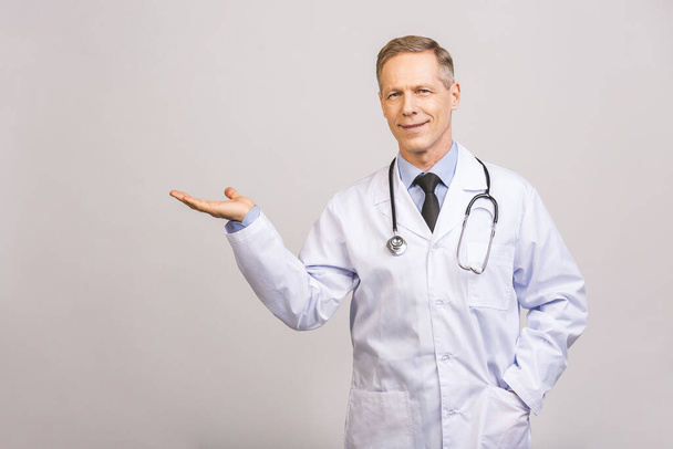 Arzt Senior, Arzt, der etwas in der leeren Hand hält, isoliert über grauem Hintergrund. - Foto, Bild