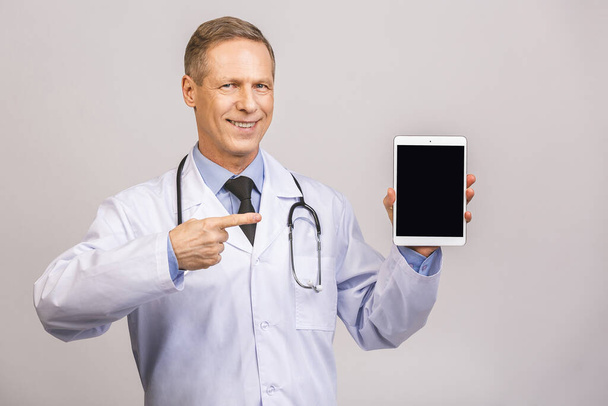 Portret starszego szczęśliwego lekarza pokazujący pusty ekran komputera na szarym tle.  - Zdjęcie, obraz
