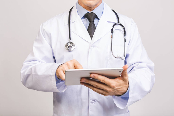 Портрет веселого улыбающегося старшего врача со стетоскопом с помощью планшета на сером фоне
. - Фото, изображение