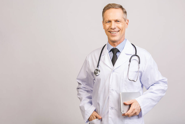 Portret wesołego, uśmiechniętego starszego lekarza ze stetoskopem i tabletką na szarym tle. - Zdjęcie, obraz