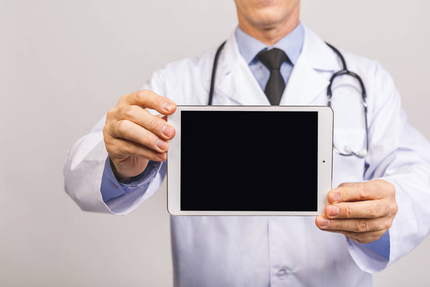 Porträt des glücklichen Oberarztes zeigt Tablet-Computer leeren Bildschirm isoliert über grauem Hintergrund.  - Foto, Bild