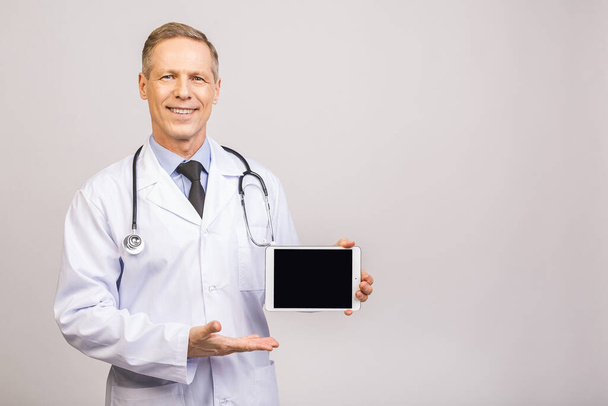 Portrait of senior happy doctor showing tablet computer blank screen isolated over grey background.  - Photo, image