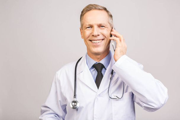 Lähikuva kuva vanhempi mies lääkäri seisoo eristetty harmaalla pohjalla, matkapuhelimella. - Valokuva, kuva