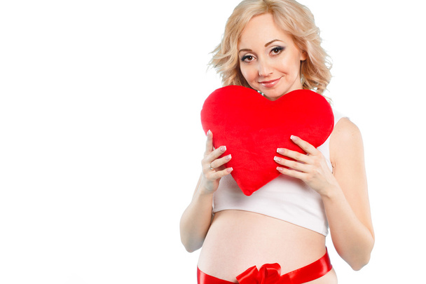 Pregnant beautiful woman holding red heart pillow in her hands isolated on white background - Foto, Bild