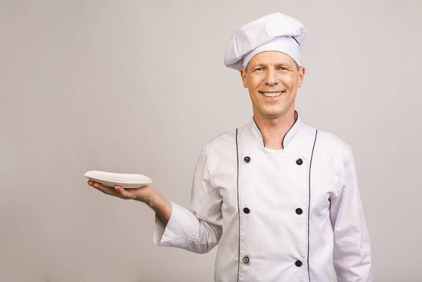 Portrét staršího kuchaře držícího prázdné jídlo izolované na bílém pozadí. - Fotografie, Obrázek