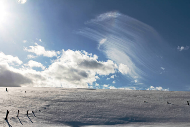 Όμορφα σύννεφα στον γαλάζιο ουρανό πάνω από ένα χιονισμένο χωράφι με φράχτες  - Φωτογραφία, εικόνα