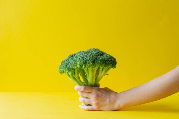 La mano femminile tiene i broccoli su uno sfondo giallo. Alimentazione sana concetto - Foto, immagini