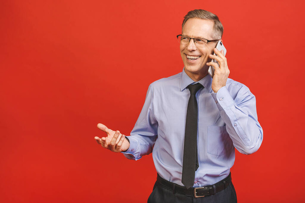 Relaxed senior business man in formal using smartphone isolated on red background. Portrait of a happy mature businessman using cell phone. Satisfied leader checking mail with copy space. - Foto, imagen
