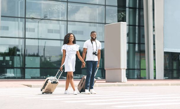 Feliz afroamericano recién casados caminando fuera del edificio del aeropuerto con equipaje
 - Foto, Imagen