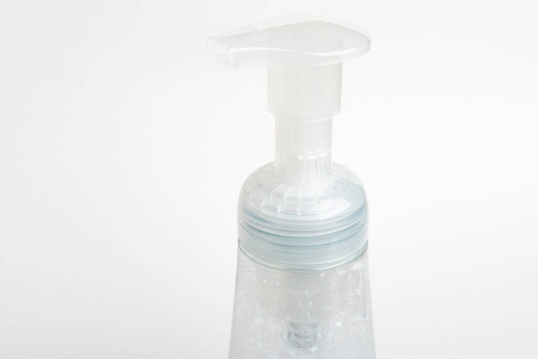 Una imagen de cerca de la bomba superior translúcida y la botella de un dispensador de plástico de jabón de espuma sobre un fondo blanco
. - Foto, imagen