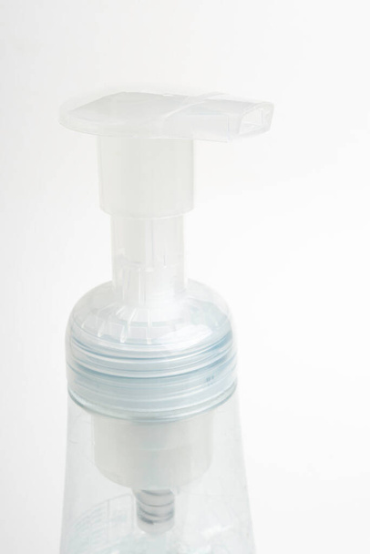 Uma imagem de close-up da bomba superior translúcida e garrafa de um dispensador de plástico de sabão de espuma em um fundo branco
. - Foto, Imagem