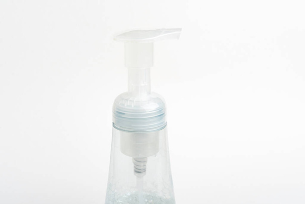 Una imagen de cerca de la bomba superior translúcida y la botella de un dispensador de plástico de jabón de espuma sobre un fondo blanco
. - Foto, Imagen