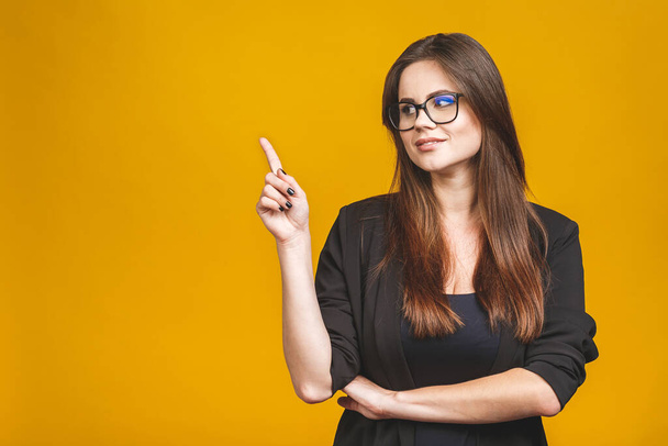 Portrait of smiling young business woman pointing up and looking at the camera isolated against yellow background. - Foto, Bild