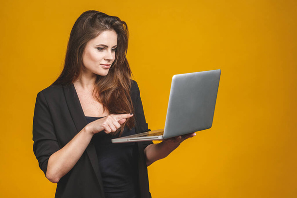 jong gelukkig glimlachen vrouw in casual kleding holding laptop en het verzenden van e-mail naar haar beste vriend geïsoleerd tegen gele achtergrond.  - Foto, afbeelding