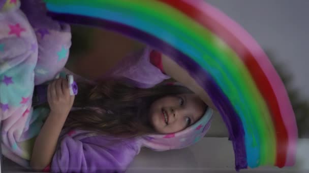 vídeo vertical. menina da escola em pijama desenha o arco-íris na janela em casa. Fique em casa, flash mob perseguir o arco-íris
 - Filmagem, Vídeo