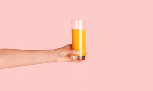 Close up of girl hand holding glass of orange juice on pink background, panorama - Fotó, kép