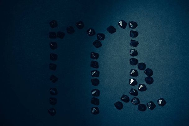 Symbol des Tierkreiszeichens Jungfrau aus schwarzen Steinen auf schwarzem Hintergrund. Niedrige Dunkelziffer. Vignettenbeleuchtung. Horoskop-Thema - Foto, Bild
