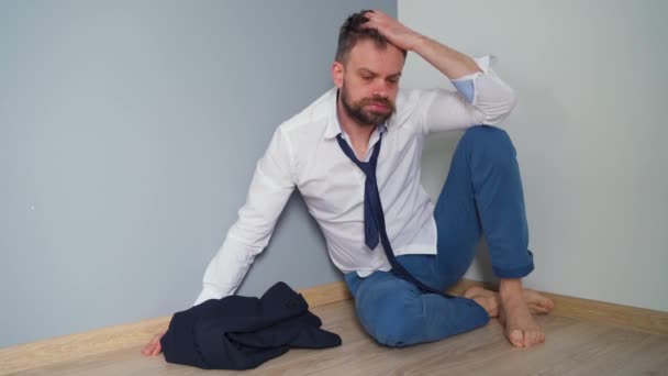 Feldúlt szakállas férfi rendetlen formális ruhákban fekszik a padlón egy üres lakásban. A Covid-19 vírus hatása a gazdaságra a munkanélküliség, a szegénység és a betegség.. - Felvétel, videó