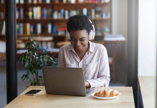Afrikkalainen amerikkalainen bloggaaja kuulokkeet ja kannettava tietokone kommunikoi seuraajia kahvilassa - Valokuva, kuva