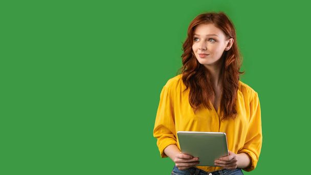 Millennial menina segurando tablet computador olhando para fora no fundo verde
 - Foto, Imagem