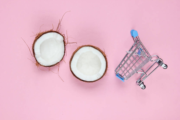 Koncepcja zakupów owoców. Wózek sklepowy, połówki połamanego kokosa na różowym tle. Widok z góry - Zdjęcie, obraz