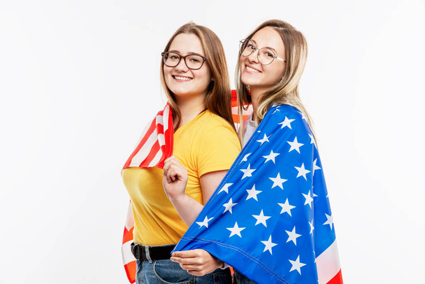 Le ragazze in jeans tengono la bandiera americana, abbracciano e ridono. Festeggiamo il giorno dell'indipendenza e il patriottismo. Isolato su uno sfondo bianco. Spazio per testo
. - Foto, immagini