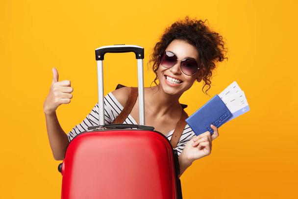 Ragazza turistica in posa con valigia gesticolando Pollici in su, sfondo giallo
 - Foto, immagini