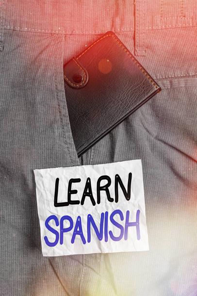 Text sign showing Learn Spanish. Conceptual photo to train writing and speaking the national language of Spain Small little wallet inside man trousers front pocket near notation paper. - Photo, Image
