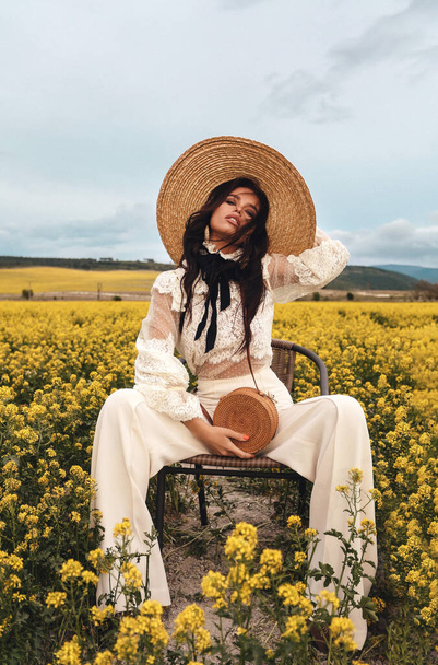 foto de moda de la hermosa mujer sexy con el pelo oscuro en ropa elegante posando en el campo con flores de flor amarilla
 - Foto, imagen