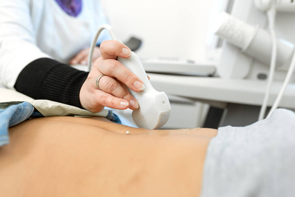Close-up doctor conducts ultrasound diagnostics of the patients abdomen and internal organs. - Foto, afbeelding