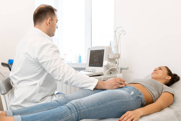 Ultrasound diagnosis of the pelvic organs of the girl. A girl lies on a couch in a white room of ultrasound diagnostics during a diagnostic. - Photo, image
