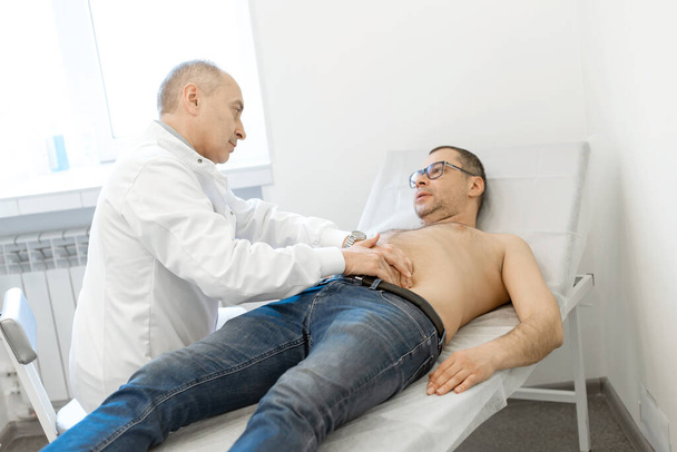 Doctor therapist probes the stomach of a male patient who is lying on a couch. Professional medical advice. - 写真・画像