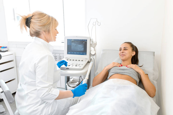 婦人科医はソファに横たわっている患者を診断するために超音波装置を設置します。骨盤内臓器の経膣超音波スキャナー。女性の健康コンセプト. - 写真・画像