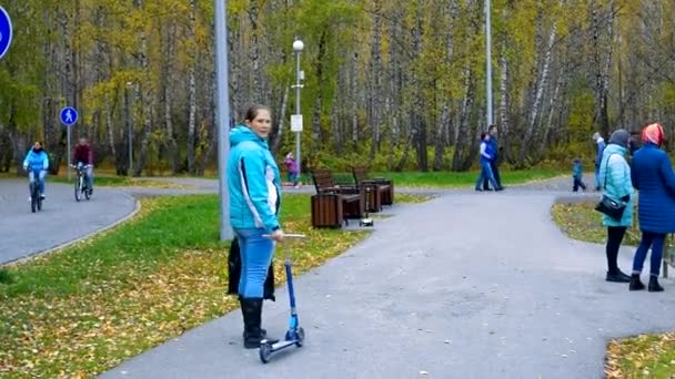 woman mother holds small scooter child runs on park track - Felvétel, videó