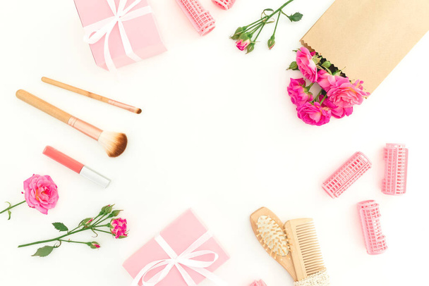 Schönheitsrahmen aus rosa Rosen mit Haarbürste, Quaste und Geschenkbox auf weißem Hintergrund. Flache Lage, Draufsicht - Foto, Bild