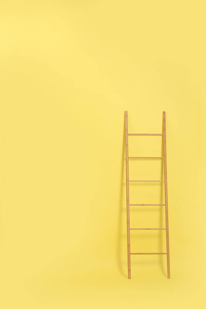 Moderne houten ladder op gele achtergrond. Ruimte voor tekst - Foto, afbeelding