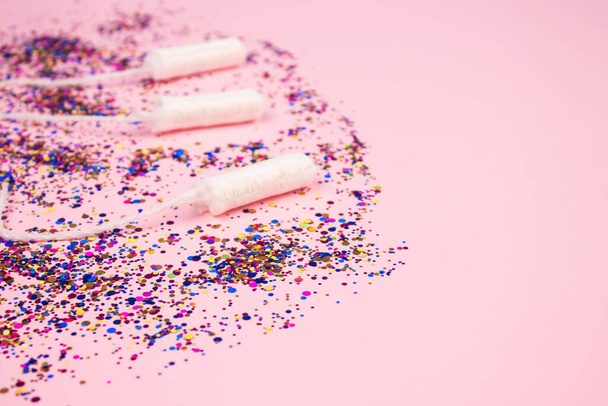 Set van schone katoenen tampons met kleurrijke sprankelingen op pastelroze achtergrond met copyspace voor je creatieve ontwerp - kritische dagen en menstruatieconcept. Vlak leggen voor de menstruatiedag - Foto, afbeelding